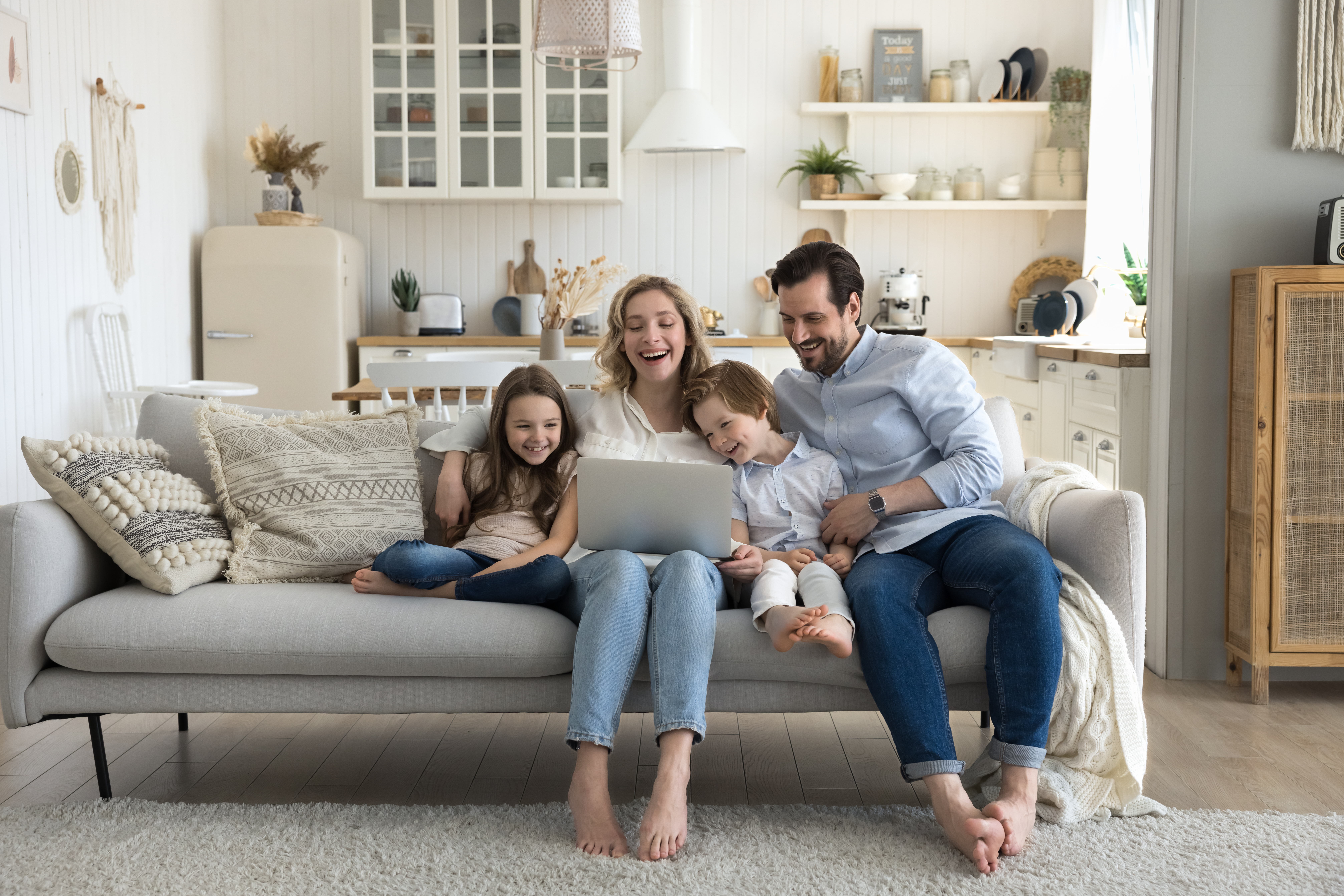 Two cheerful little kids, happy mom and dad enjoying leisure at home together, using laptop on sofa, talking on video call, laughing, watching movie, interactive online TV channel