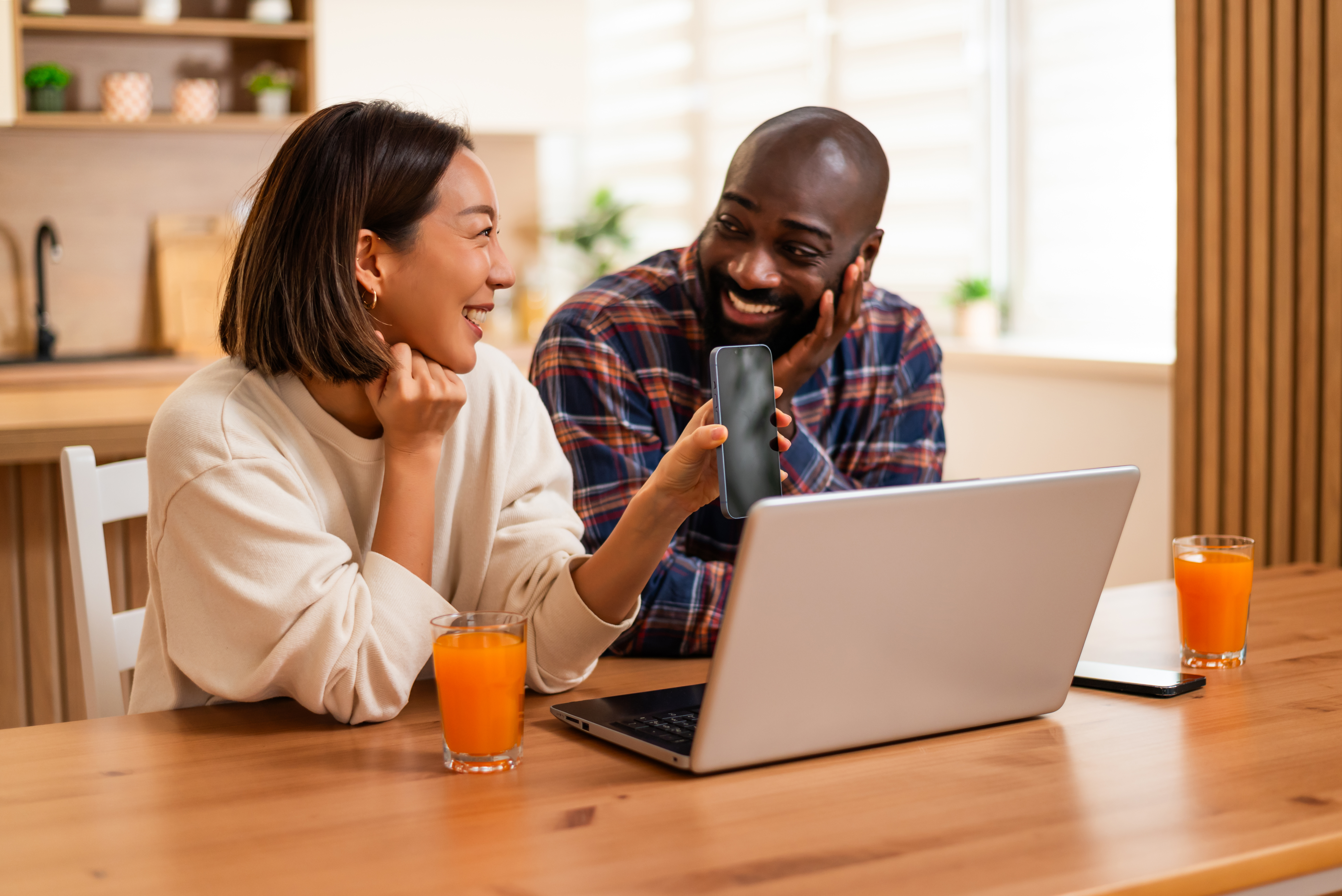 Two partners laugh together while using a laptop at home, they have a video call.