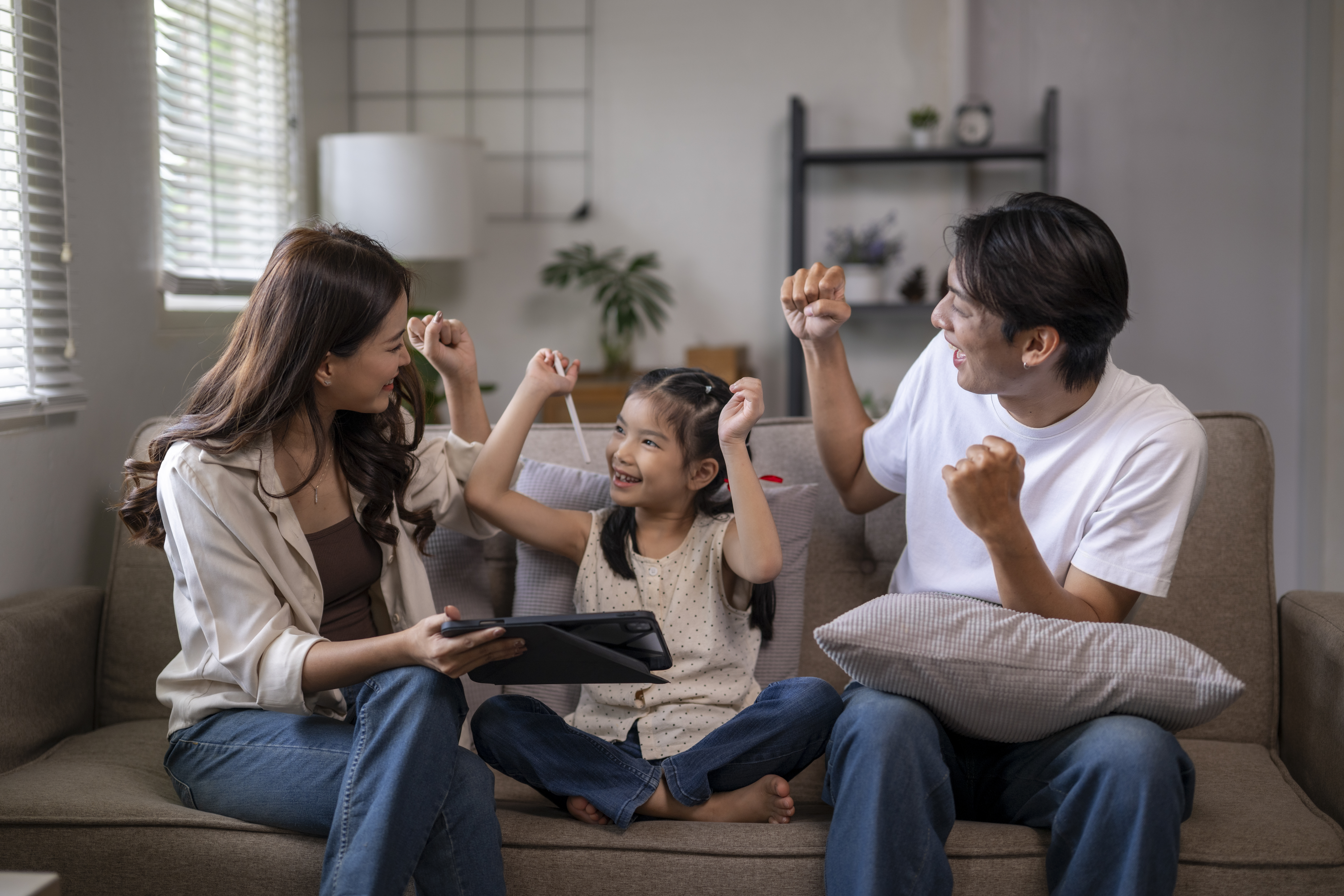 Happy family cheering and feeling excited while sitting on a sofa and using a tablet